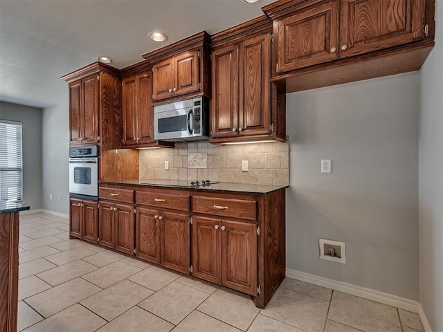 kitchen with light tile patterned floors, appliances with stainless steel finishes, tasteful backsplash, and dark stone countertops