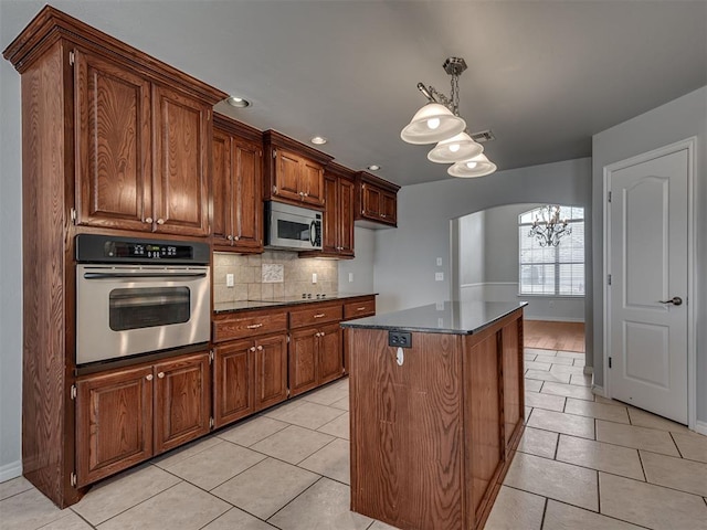 kitchen with appliances with stainless steel finishes, a center island, tasteful backsplash, an inviting chandelier, and light tile patterned floors