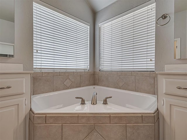 bathroom featuring tiled bath, a wealth of natural light, and vanity