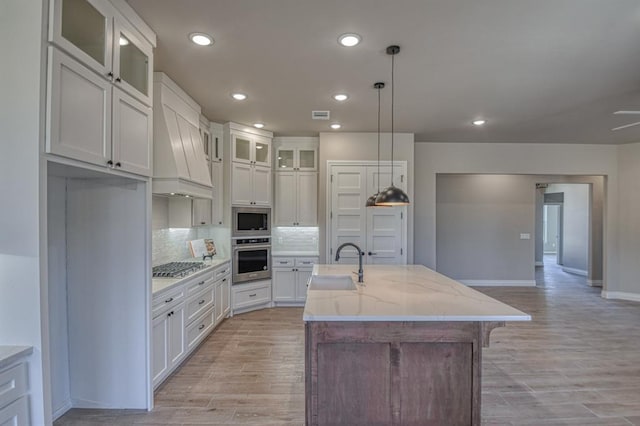 kitchen with white cabinetry, a center island with sink, stainless steel appliances, decorative light fixtures, and light stone counters