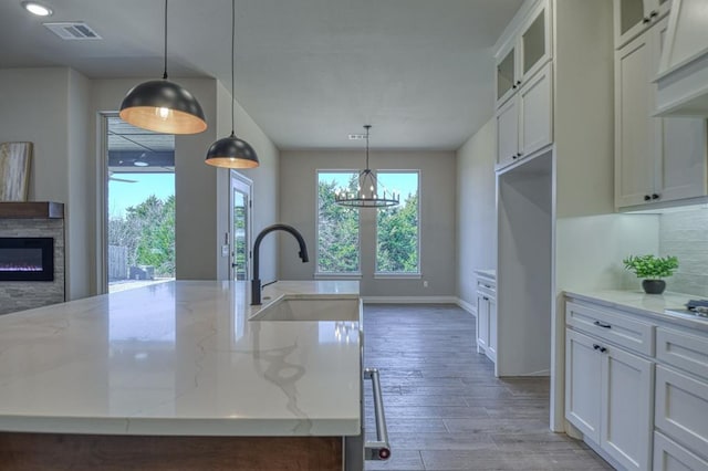 kitchen featuring an island with sink, a chandelier, pendant lighting, white cabinets, and light stone counters