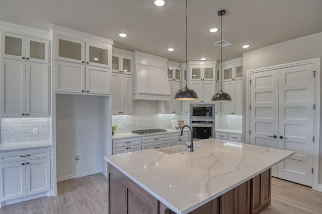 kitchen with white cabinetry, stainless steel appliances, decorative light fixtures, a kitchen island with sink, and sink