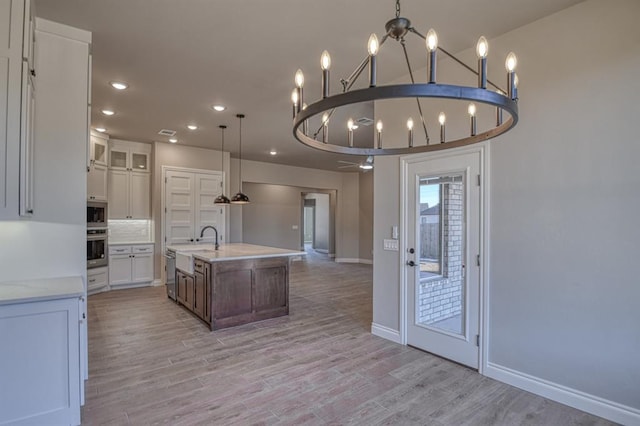 kitchen featuring a center island with sink, light wood-type flooring, hanging light fixtures, a chandelier, and white cabinets