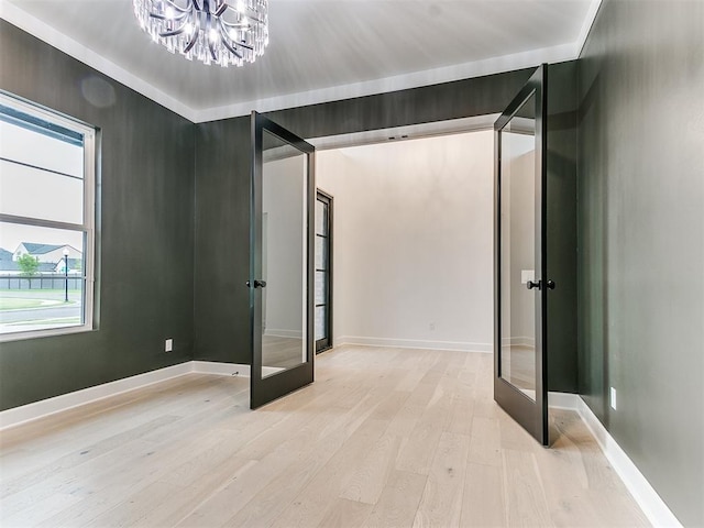 unfurnished bedroom featuring french doors, a chandelier, and light hardwood / wood-style flooring