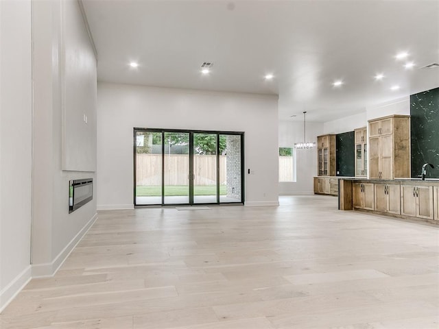 unfurnished living room featuring a healthy amount of sunlight, light wood-type flooring, heating unit, and sink