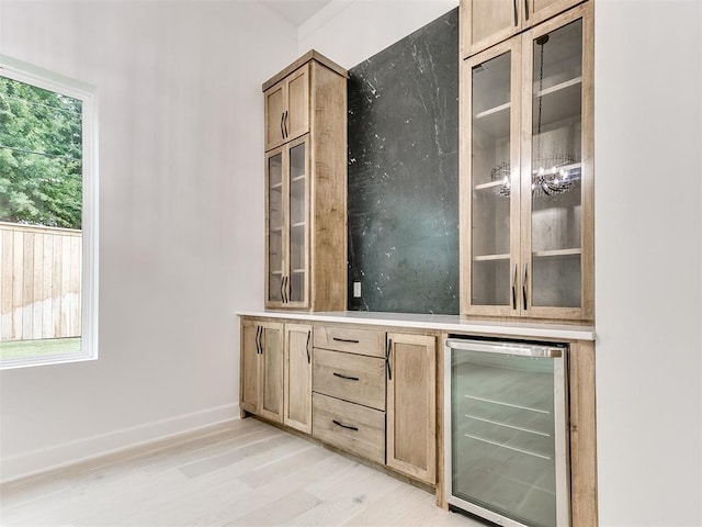 bar with light hardwood / wood-style floors, beverage cooler, and light brown cabinetry