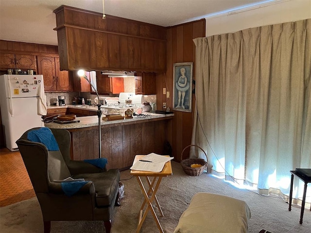 kitchen with kitchen peninsula, wooden walls, light carpet, white refrigerator, and range