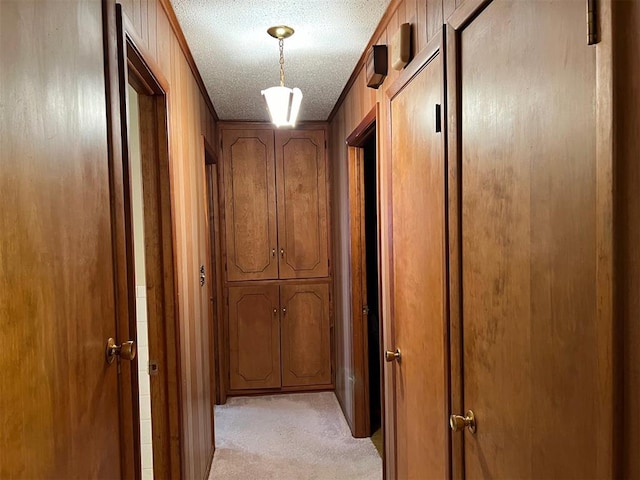 corridor featuring wood walls, a textured ceiling, and light carpet