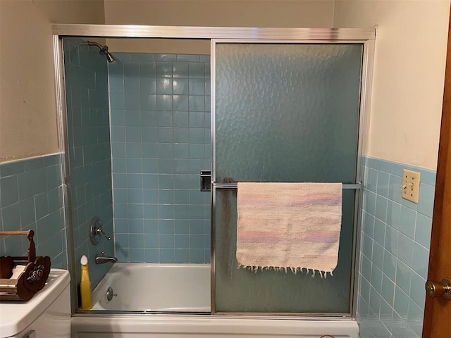 bathroom with tile walls, shower / bath combination with glass door, and toilet