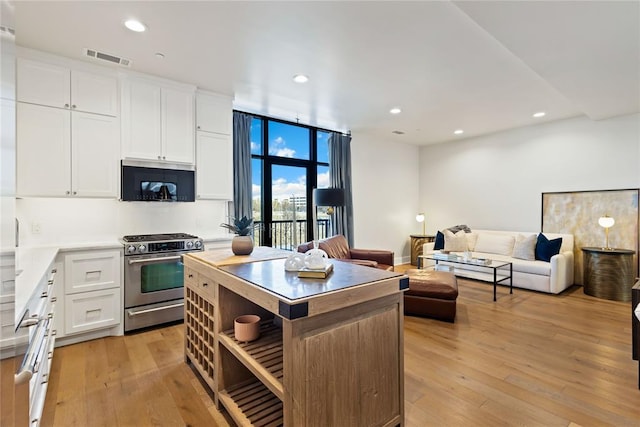 kitchen with white cabinets, light wood-type flooring, a center island, and stainless steel range with gas cooktop