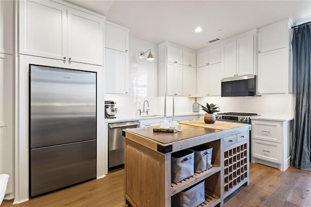 kitchen with a kitchen island, light wood-type flooring, white cabinetry, appliances with stainless steel finishes, and sink