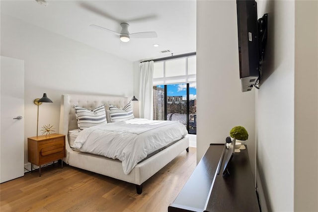 bedroom with a wall of windows, hardwood / wood-style flooring, ceiling fan, and access to outside