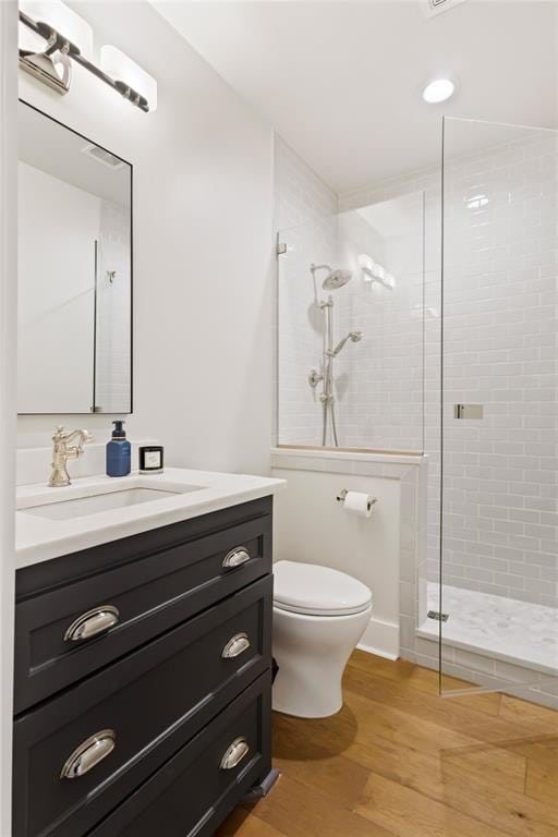 bathroom with a tile shower, vanity, toilet, and hardwood / wood-style floors