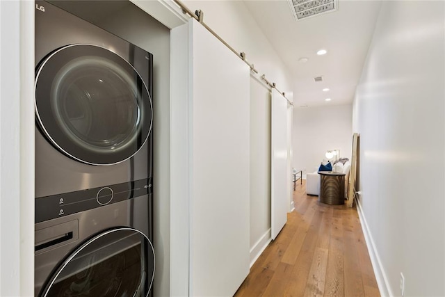 laundry area featuring light hardwood / wood-style flooring, stacked washer / dryer, and a barn door