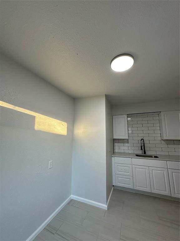 kitchen with sink, white cabinets, a textured ceiling, and backsplash