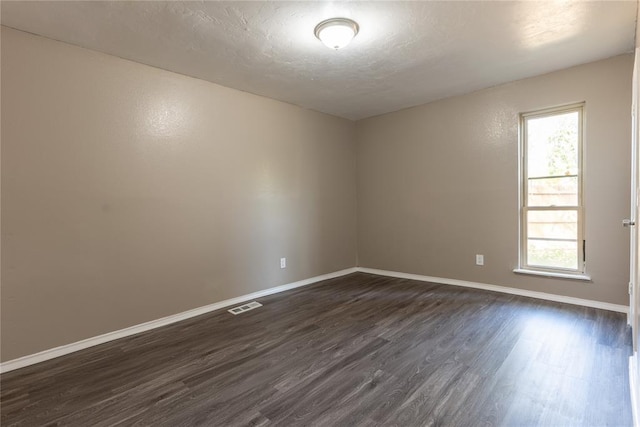 empty room with a textured ceiling, dark hardwood / wood-style floors, and a healthy amount of sunlight