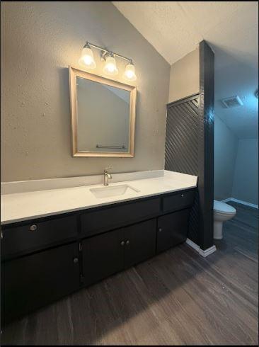 bathroom with hardwood / wood-style floors, toilet, vaulted ceiling, and vanity