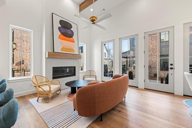 living room featuring a tiled fireplace, a wealth of natural light, light hardwood / wood-style floors, and beam ceiling