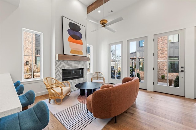 living area with a tiled fireplace, ceiling fan, a wealth of natural light, and beamed ceiling