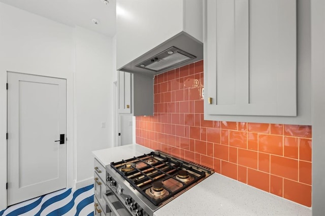 kitchen featuring stainless steel range with gas stovetop, light stone countertops, decorative backsplash, white cabinetry, and exhaust hood