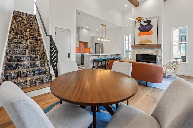 dining space with ceiling fan, light wood-type flooring, a tile fireplace, and a towering ceiling