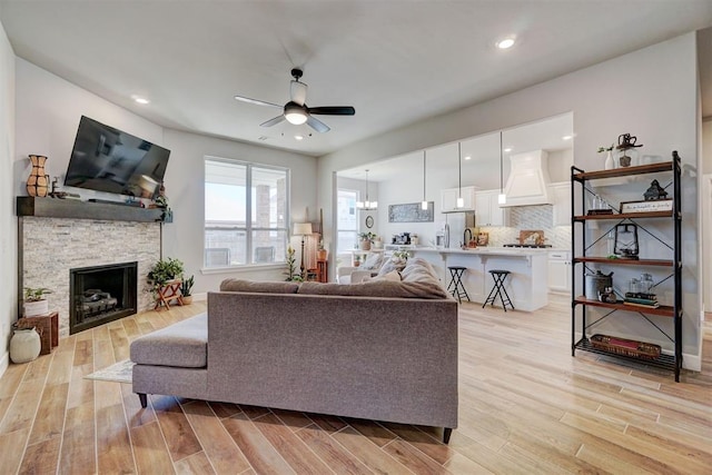 living room featuring a fireplace, ceiling fan, and light hardwood / wood-style floors