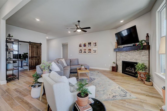 living room with ceiling fan, a stone fireplace, and a barn door