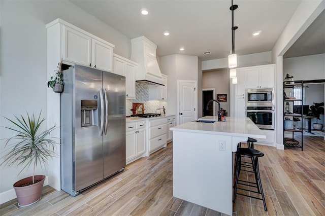 kitchen featuring custom exhaust hood, decorative light fixtures, a center island with sink, appliances with stainless steel finishes, and sink