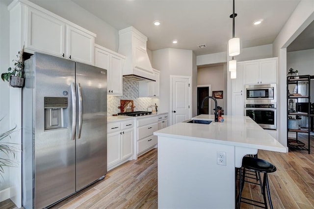 kitchen featuring decorative light fixtures, white cabinets, tasteful backsplash, an island with sink, and appliances with stainless steel finishes