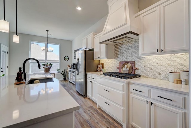 kitchen with decorative light fixtures, stainless steel appliances, custom range hood, white cabinetry, and sink