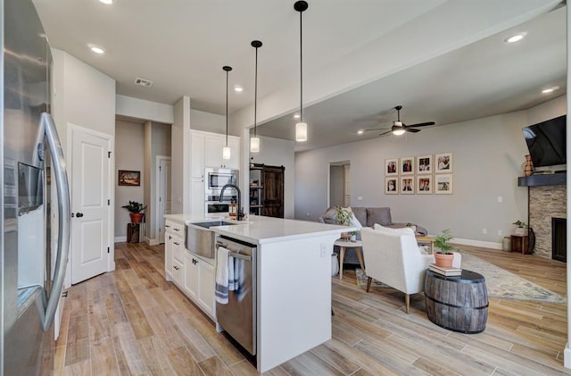 kitchen with pendant lighting, stainless steel appliances, an island with sink, white cabinets, and ceiling fan