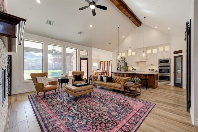 living room with ceiling fan, high vaulted ceiling, a fireplace, beamed ceiling, and light wood-type flooring