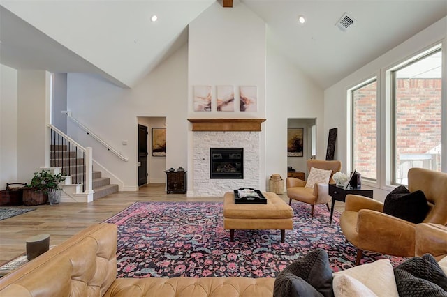 living room with a stone fireplace, high vaulted ceiling, and light hardwood / wood-style flooring