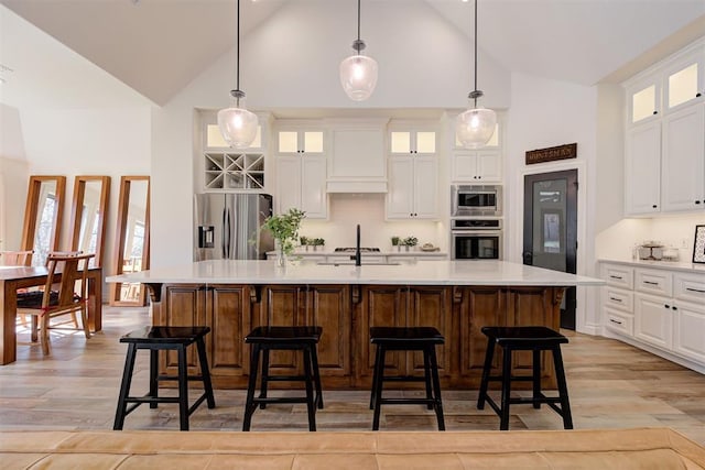 kitchen featuring white cabinetry, hanging light fixtures, custom exhaust hood, a kitchen island with sink, and stainless steel appliances