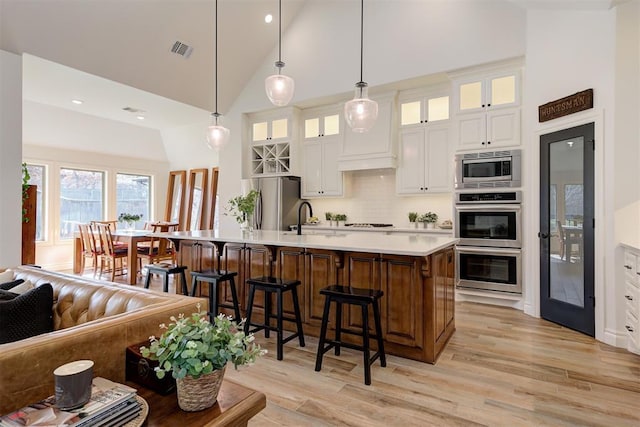 kitchen with sink, white cabinetry, pendant lighting, stainless steel appliances, and a kitchen island with sink