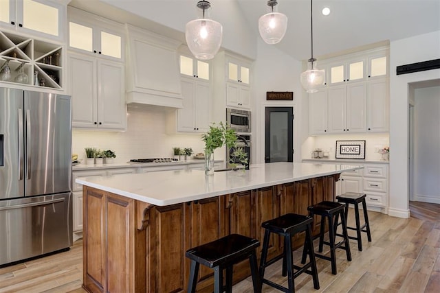 kitchen featuring white cabinetry, appliances with stainless steel finishes, a kitchen island with sink, and decorative light fixtures