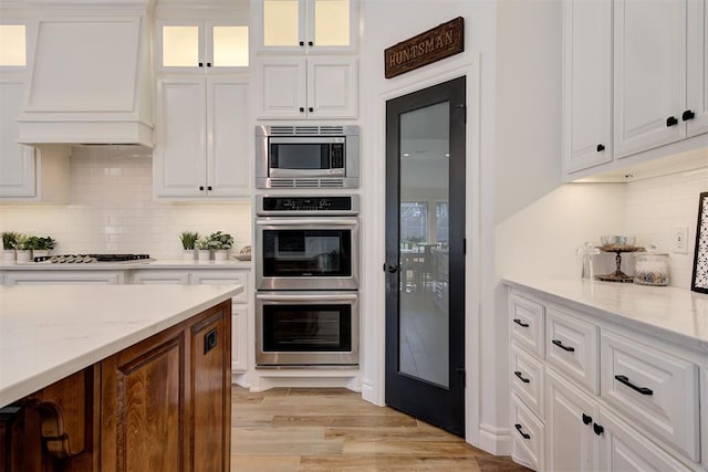 kitchen with stainless steel appliances, white cabinetry, light stone countertops, and premium range hood