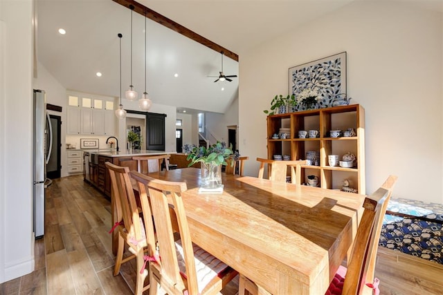 dining area with sink, high vaulted ceiling, ceiling fan, and light wood-type flooring