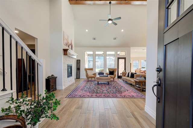 living room featuring a fireplace, light hardwood / wood-style flooring, ceiling fan, and a high ceiling