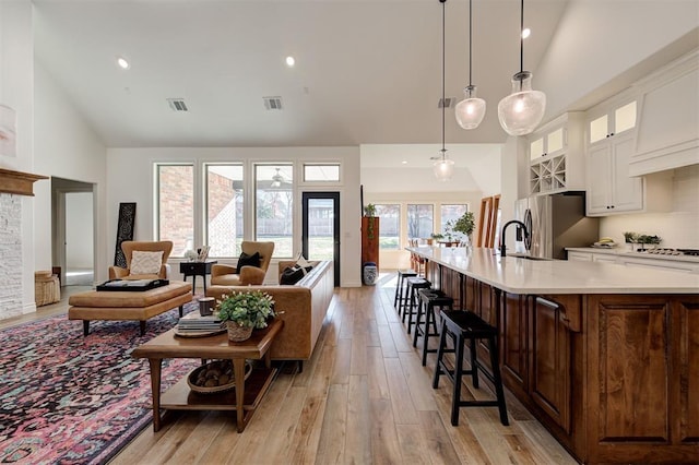 kitchen featuring pendant lighting, high vaulted ceiling, sink, stainless steel fridge, and a kitchen breakfast bar