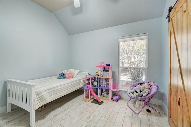 bedroom featuring ceiling fan, light wood-type flooring, a barn door, and lofted ceiling