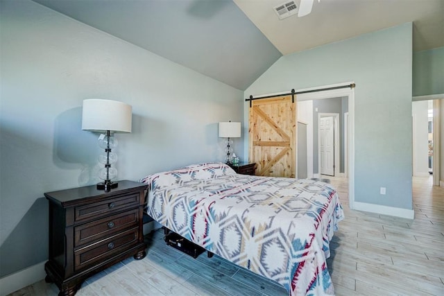 bedroom featuring light hardwood / wood-style floors, ceiling fan, vaulted ceiling, and a barn door