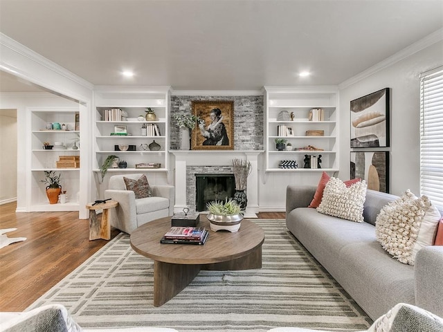 living room with built in features, a fireplace, ornamental molding, and hardwood / wood-style flooring