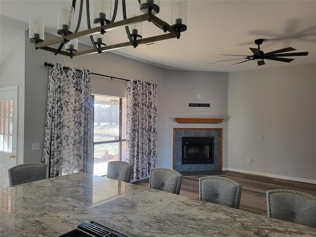 unfurnished dining area featuring dark wood-type flooring, ceiling fan with notable chandelier, and a tiled fireplace