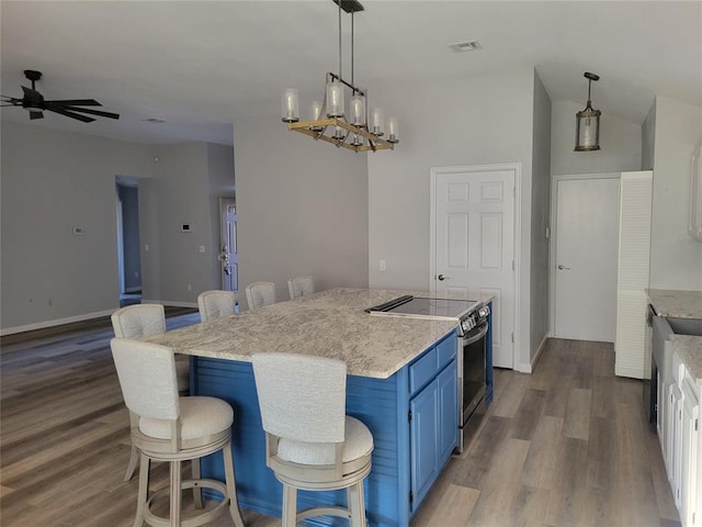 kitchen with a kitchen bar, stainless steel electric stove, blue cabinets, wood-type flooring, and a kitchen island