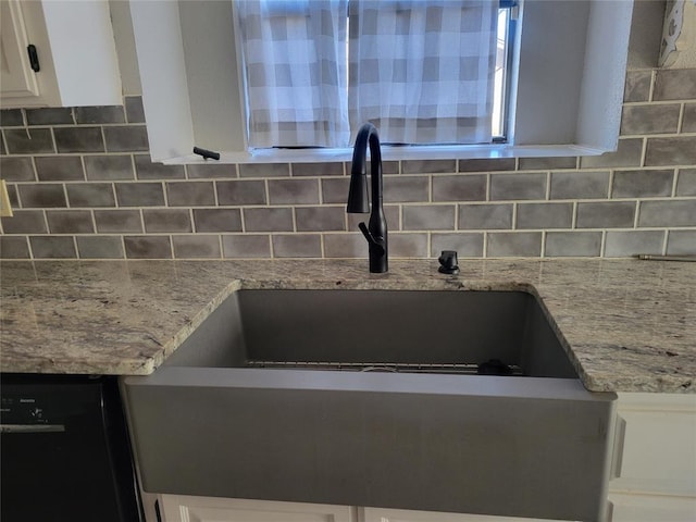 room details with light stone counters, backsplash, white cabinets, and black dishwasher