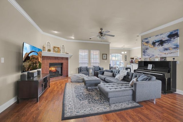 living room with crown molding, dark hardwood / wood-style flooring, ceiling fan with notable chandelier, and a brick fireplace