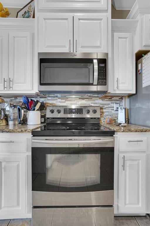 kitchen with light tile patterned flooring, appliances with stainless steel finishes, dark stone counters, decorative backsplash, and white cabinets