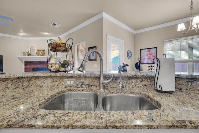 kitchen featuring pendant lighting, ornamental molding, sink, and light stone counters