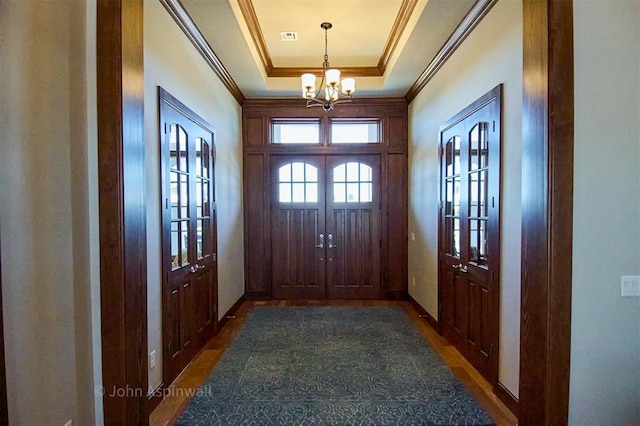 doorway featuring crown molding, a chandelier, a raised ceiling, and french doors